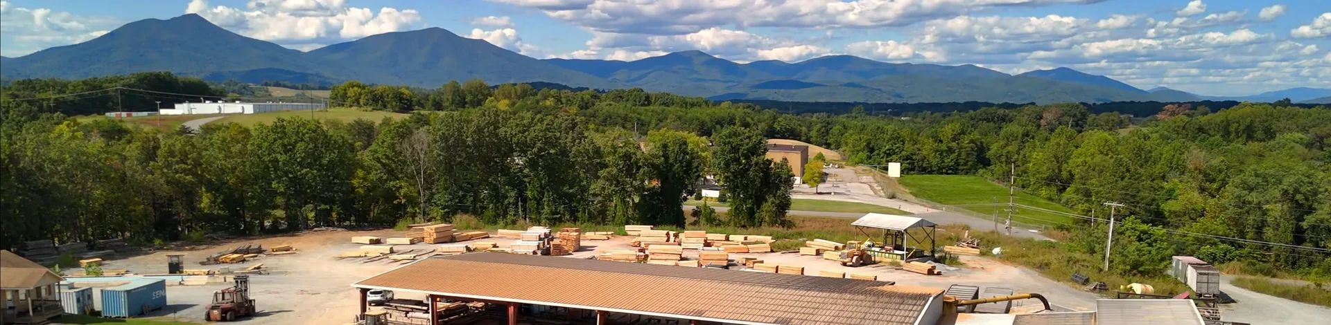 Aerial view of Turman Forest Products sawmill in Virginia with stacked hardwood lumber, front loaders, and the Blue Ridge Mountains in the background.